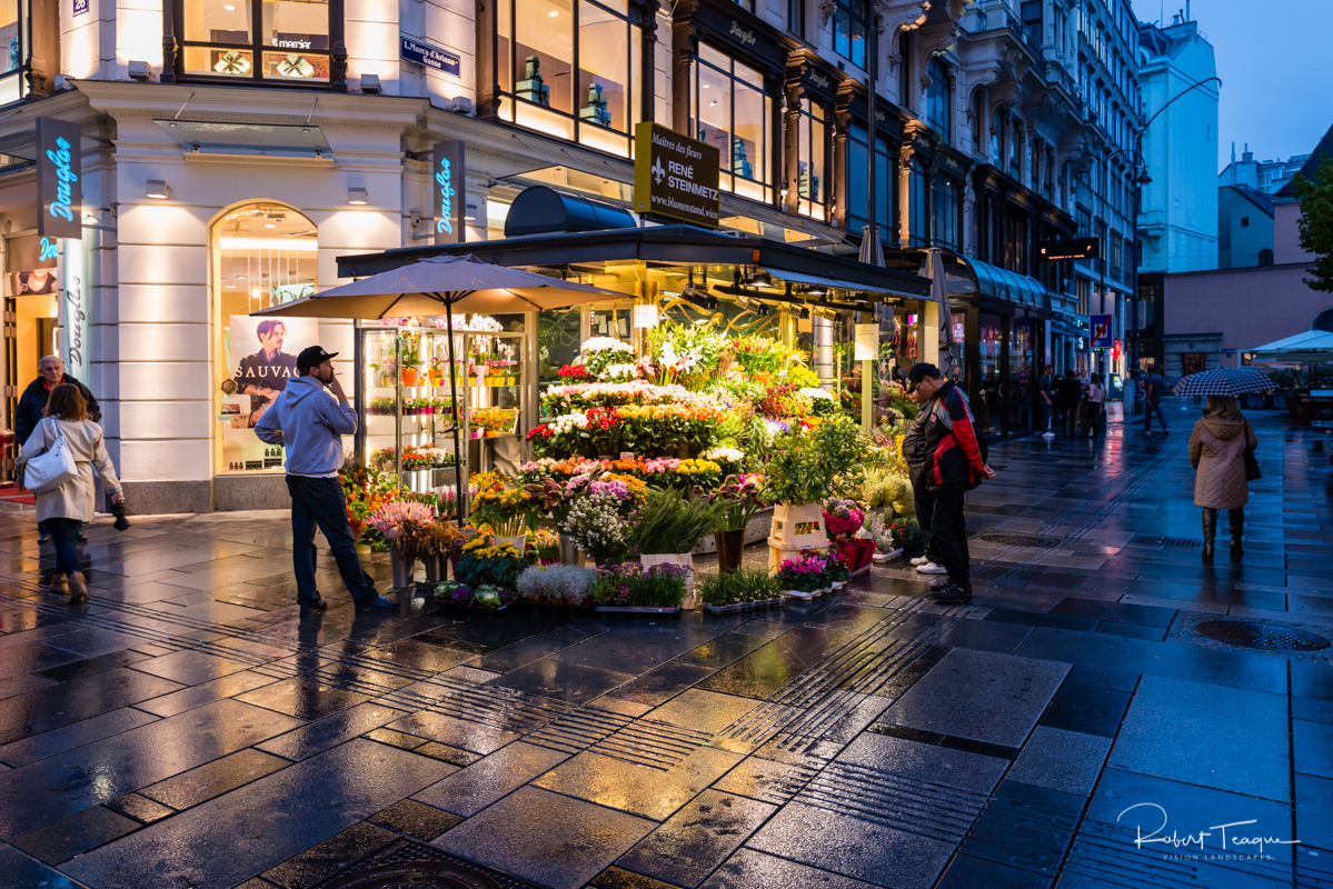 A Flower Seller pauses and smokes as shoppers look into his shop, on a rainy evening, in Innere Stadt Vienna